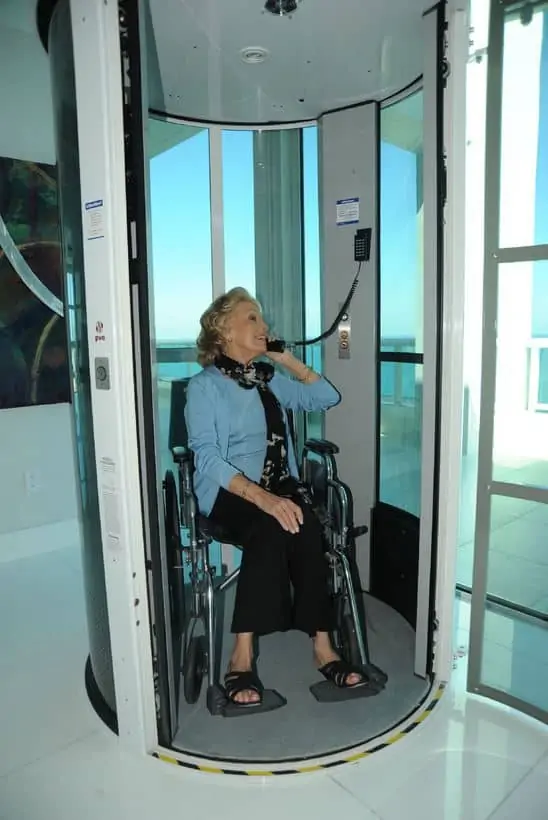 a woman in a wheelchair using the safety telephone installed in all vacuum elevators per building code